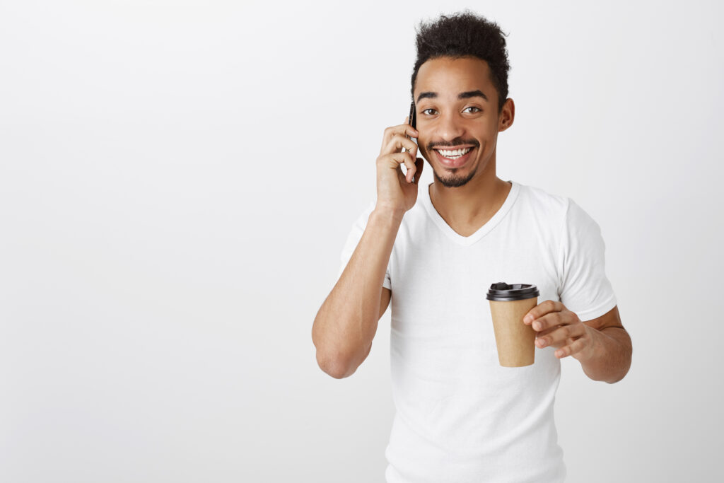 smiling attractive african american man talking phone drinking takeaway coffee